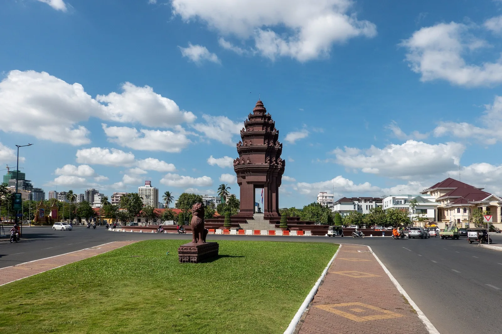 The tiered lotus-shaped Independence Monument stands on a traffic roundabout in Phnom Penh under a bright blue sky.