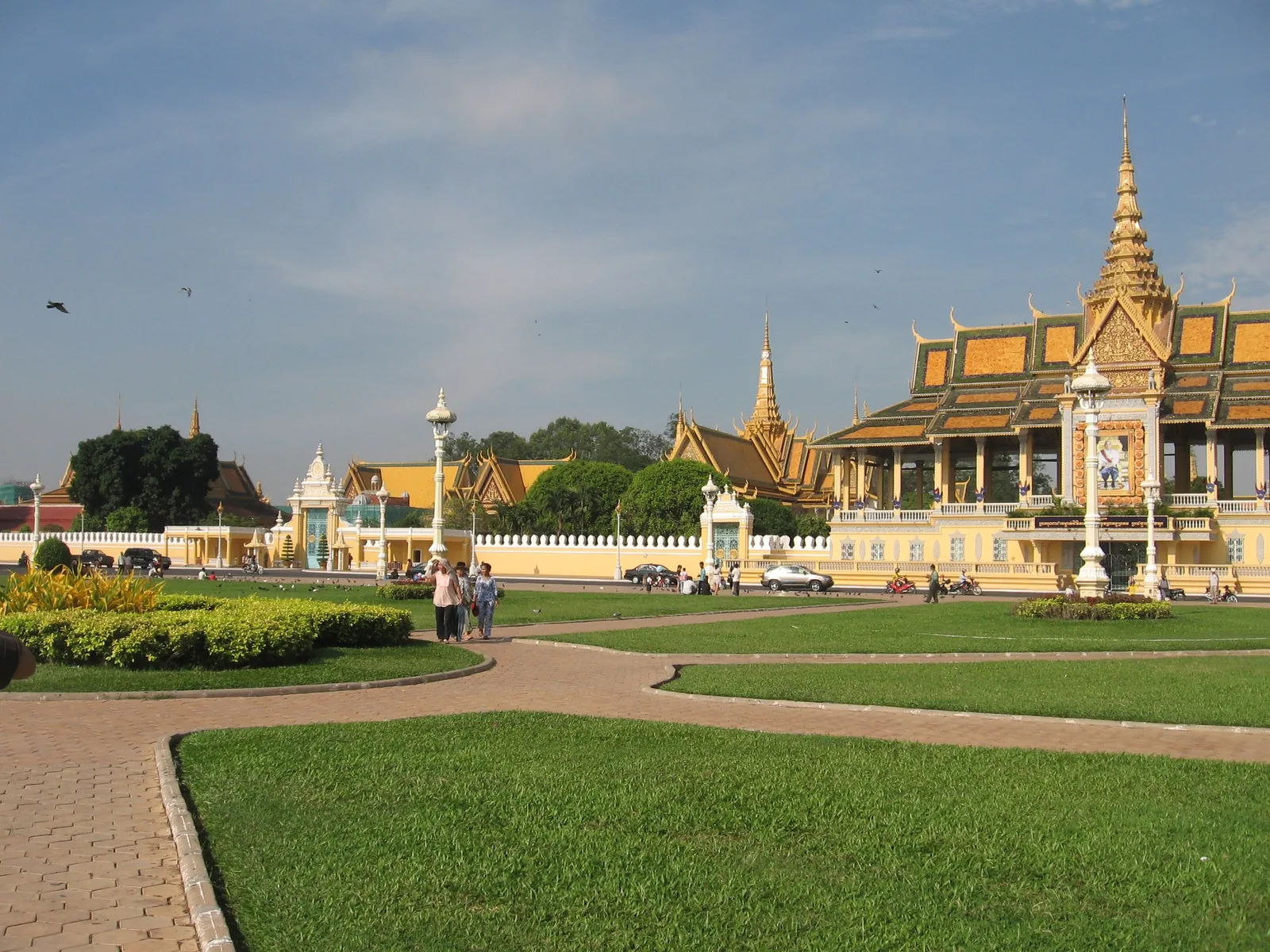 Ornate spired pavilions and green lawns at the Royal Palace complex in Phnom Penh under a blue sky.