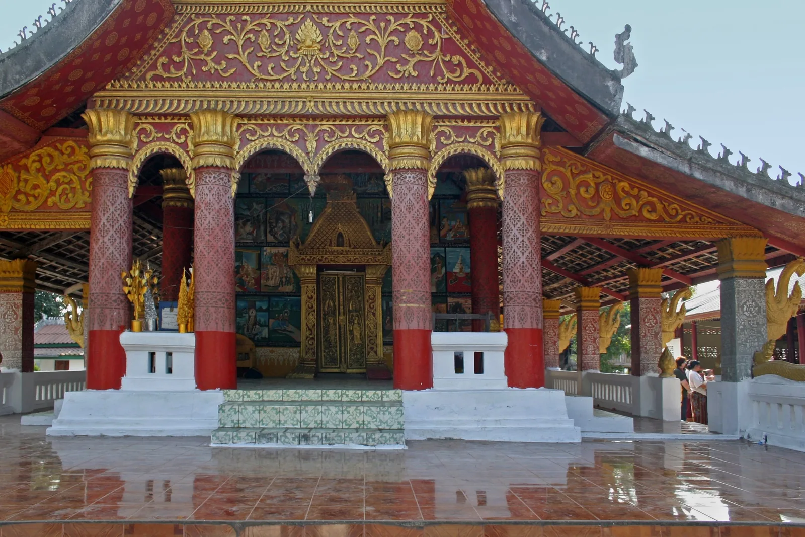 Ornate red and gold temple hall with mosaic panels and carved columns in Luang Prabang