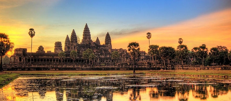 The silhouette of Angkor Wat against an orange dawn sky above the water