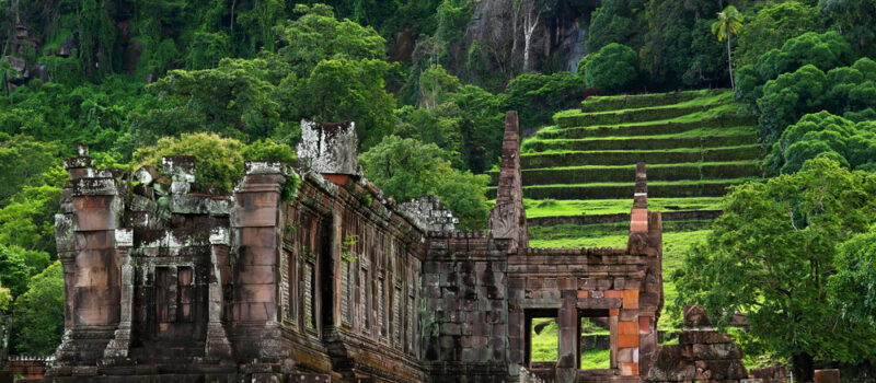 Weathered stone terraces and doorways of the Wat Phou temple below its wooded hill