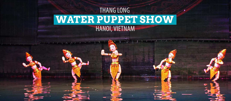 Painted wooden puppets moving across a lit water stage at a Hanoi water puppet theatre