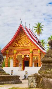 A Lao temple hall with a steep tiled roof and red and gold trim
