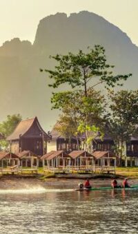 A wooden riverside pavilion under a karst hill on the bank of a Lao river