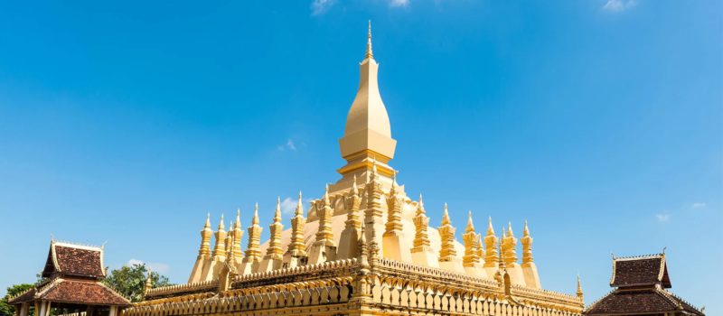 The golden spire and surrounding stupas of Pha That Luang in bright sun