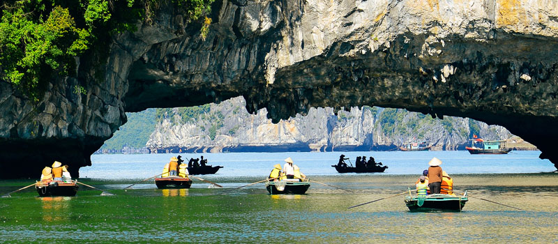 Small rowing boats carrying visitors across emerald water beneath a limestone arch